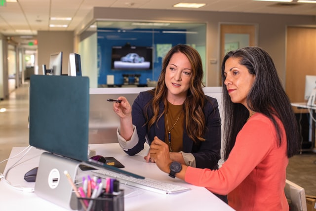 Two businesswomen talking about sales in office at desk with laptop
