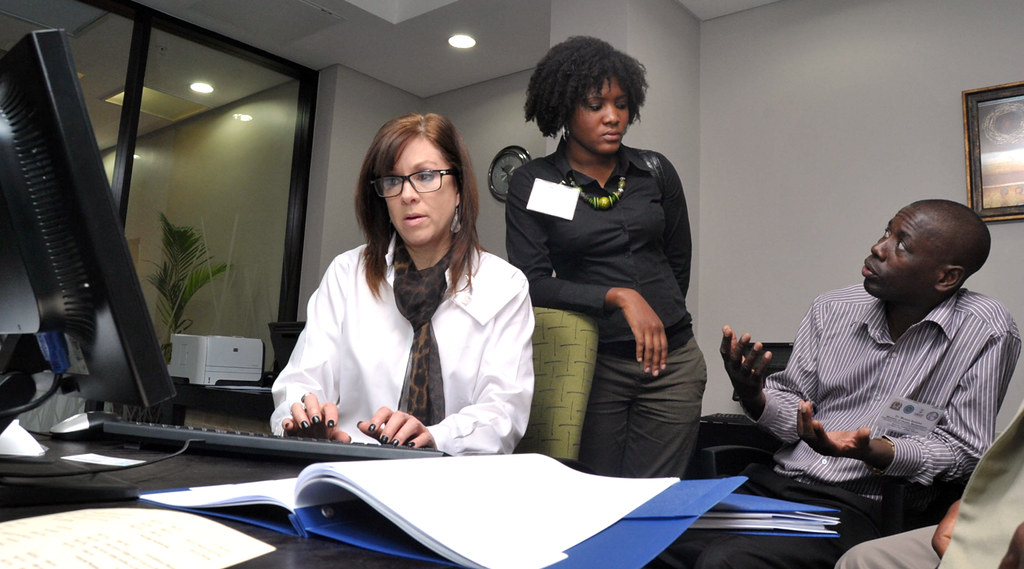 Person at computer with two people behind talking