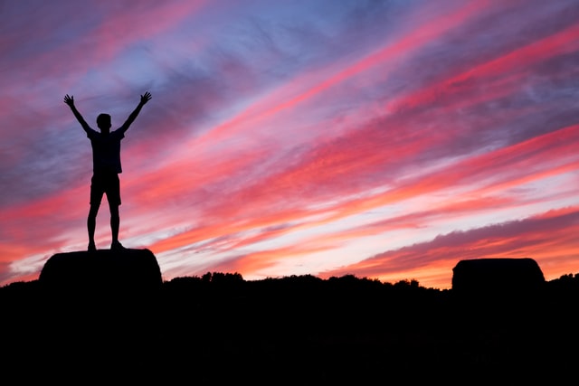 Silhouette of a person on rock in the sunset with their arms raised
