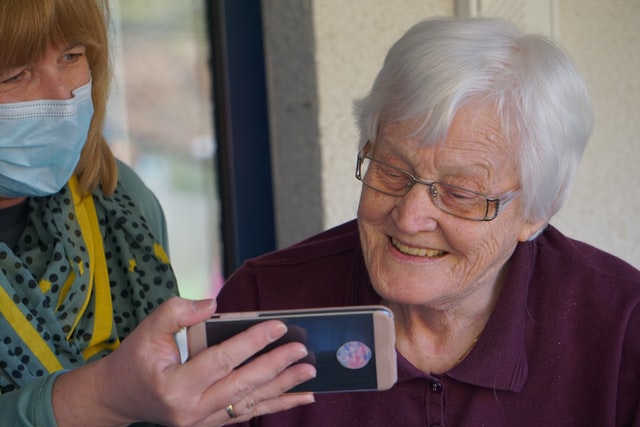 Nurse with mask looking at smart phone with elderly woman