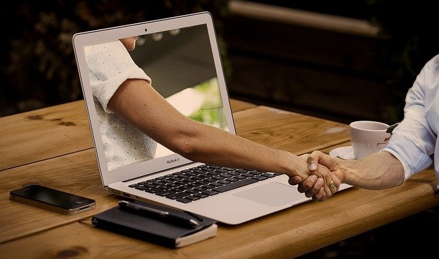 Hand reaching out of a laptop on desk to shake another