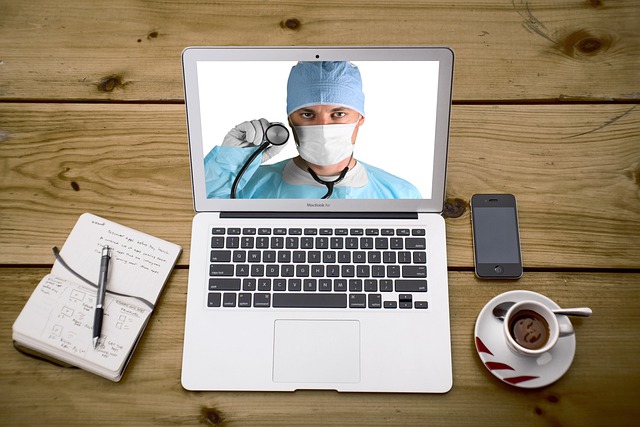 A picture of doctor with stethoscope on laptop computer on top of home desk with coffee, cell phone and notebook to depict telemedicine/virtual appointment.