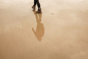 Person walking on beach. Their reflection is shown in the water.