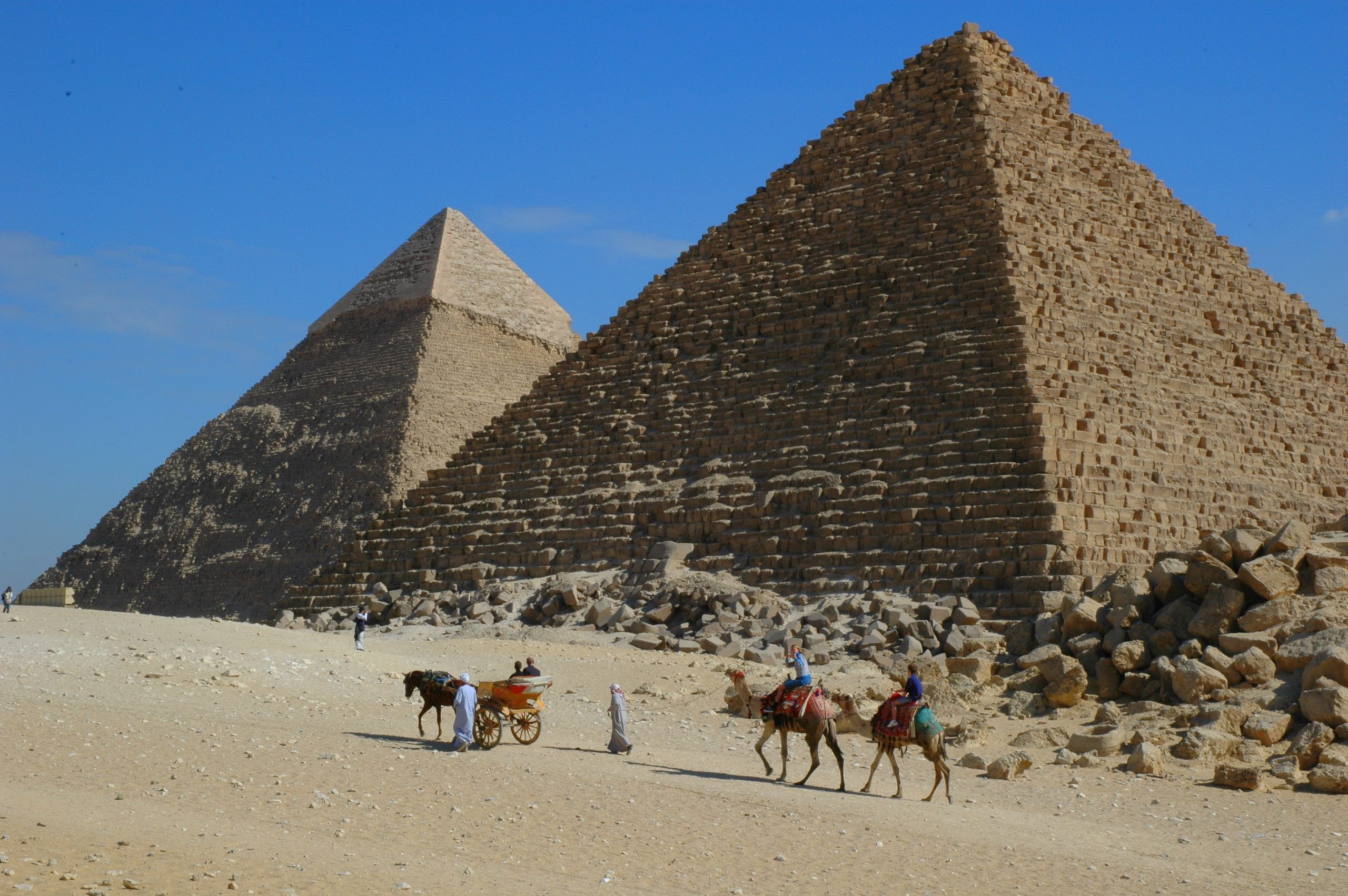 The image is a photograph of people riding camels in front of two pyramids in Egypt.