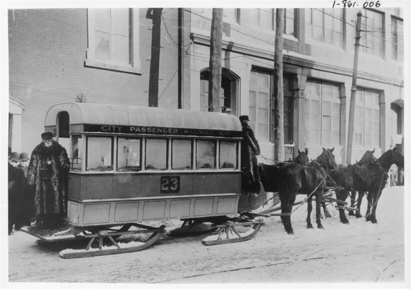 Four horses pull a tram on sled runners in the city.