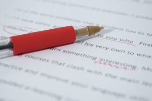 A red pen sits on top of paper that has been corrected in red pen