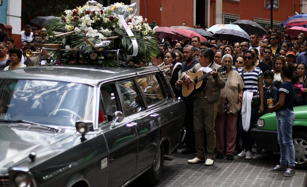 Farewell Serenade in the streets of Guanajuato, Mexico. A group of people led by a guitarist follow a hearse laden with white flowers.