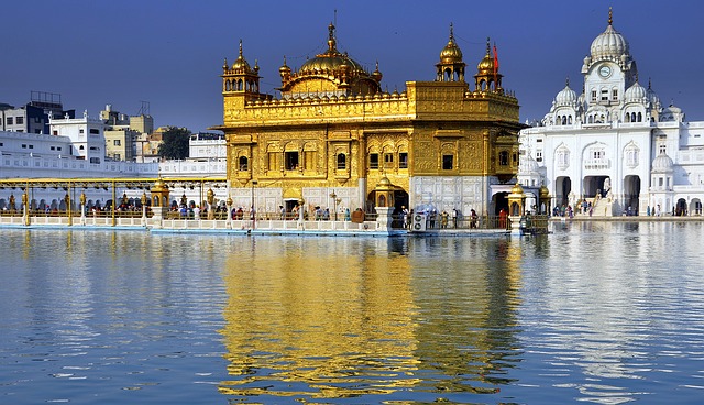 Amritsar Golden Temple reflecting in the water, with people in the front of the temple.