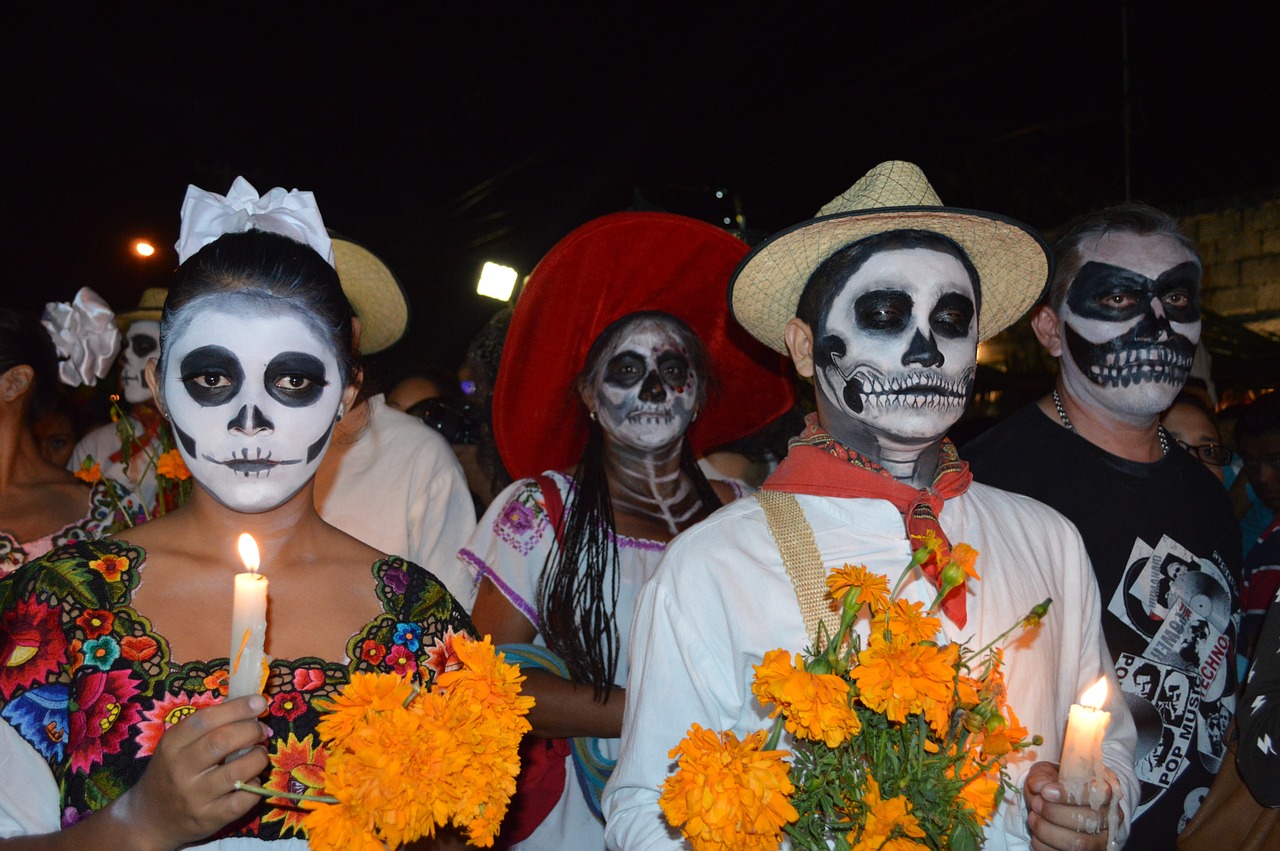 Mexican people with skeleton makeup holding candles and flowers to celebrate Day of the Dead