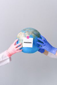 Hands with latex gloves holding a globe. Taped on the globe is a square memo with "pandemic" printed on it