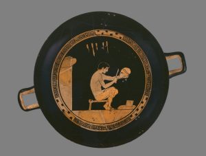 A single man shaping a helmet in a small workshop with tools hung on the wall behind him.