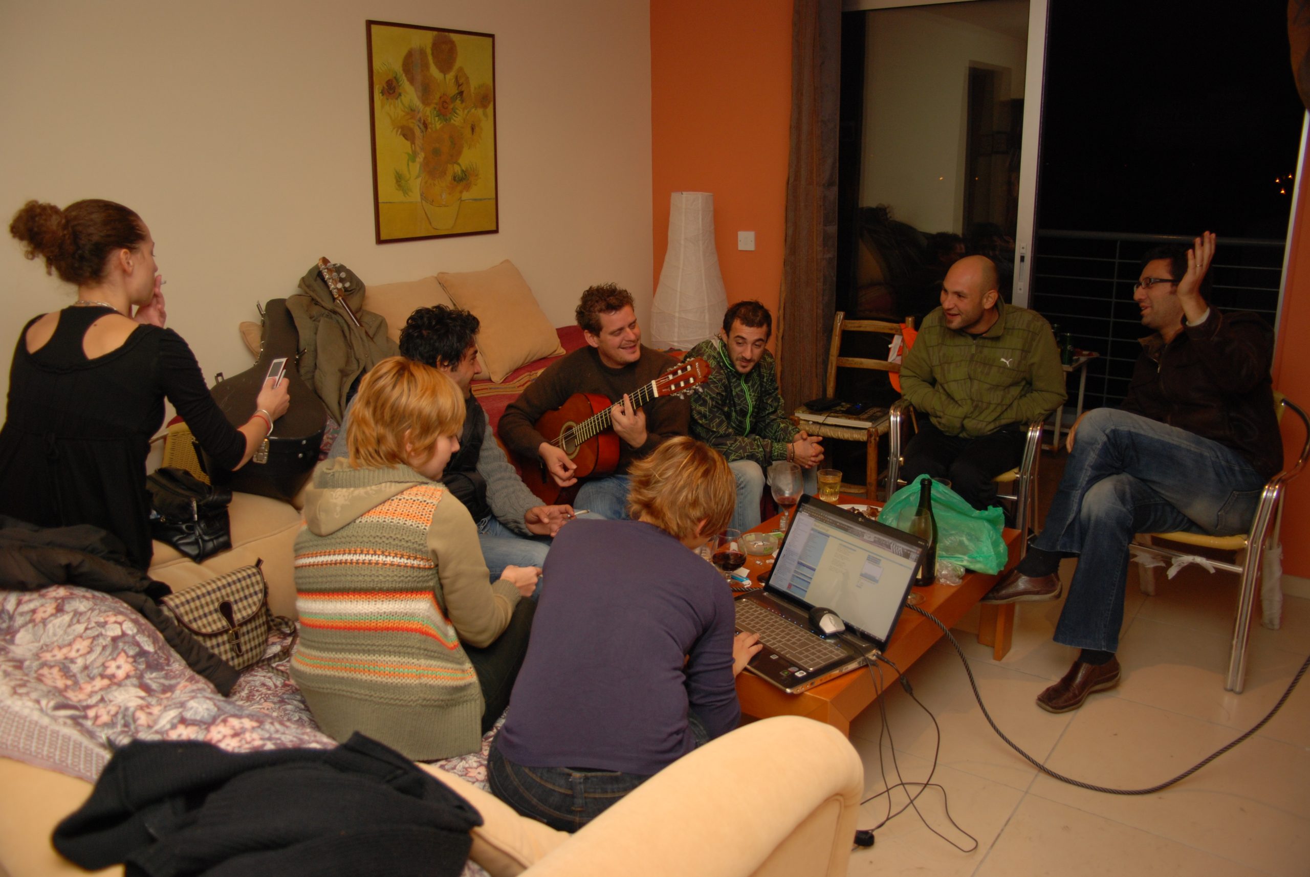 Friends seated in a living room. Someone is playing the guitar.