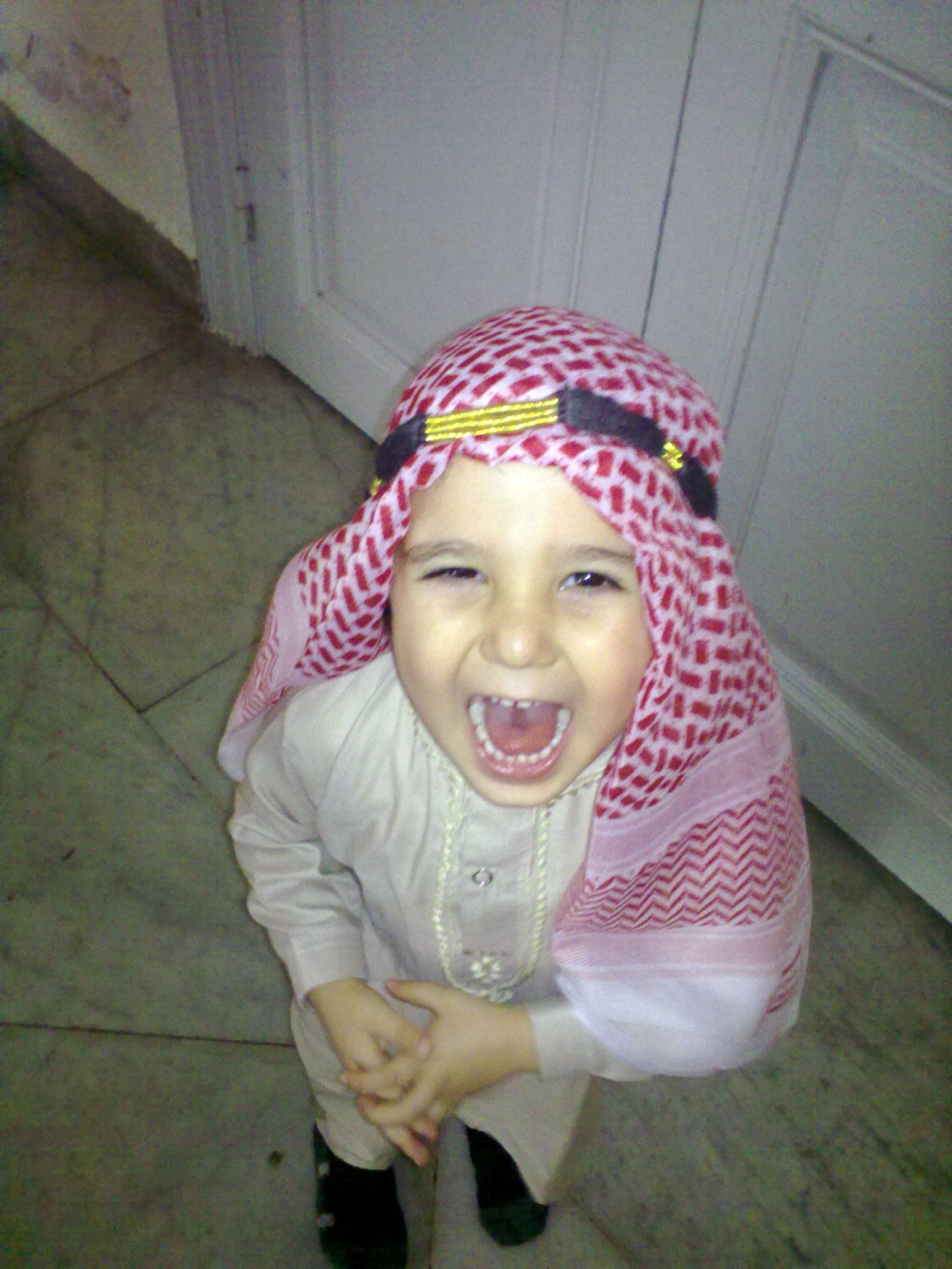 Photo of a young boy, laughing, in traditional arabic attire.