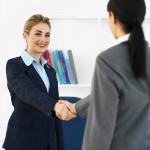 Two woman wearing business attire and shaking hands
