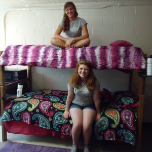 Two college students sit on bunk beds in a very clean and orderly dorm room.