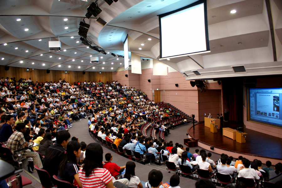 Instructeur présentant à des centaines d'étudiants dans une grande salle de conférence.