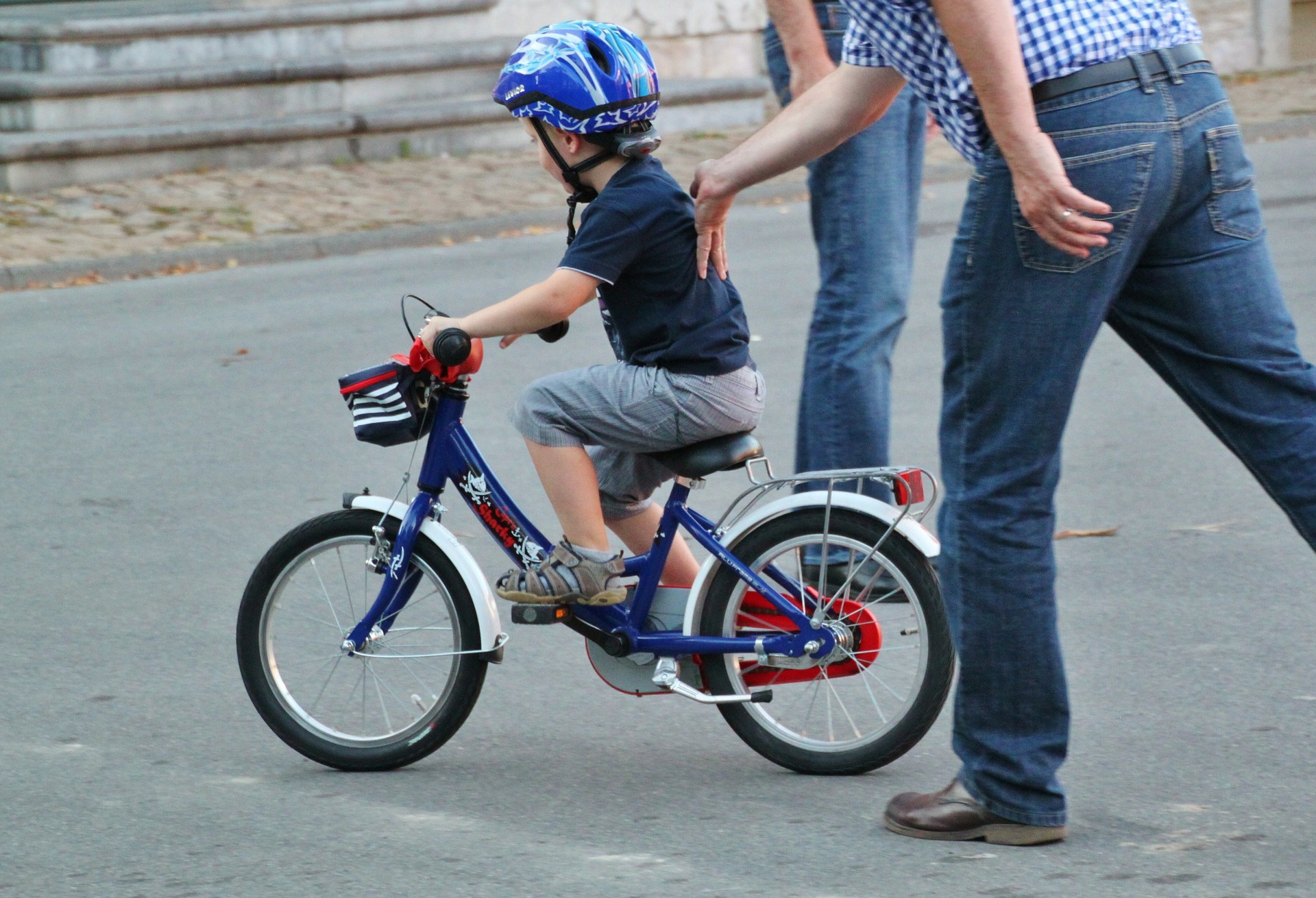 Man supports a child learning how to ride a bike.
