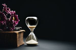 Timeglass beside a wooden box with flowers.