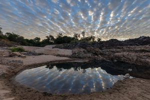 Water_reflection_of_stringy_gray_and_white_clouds_in_a_pond_on_a_sand_beach_of_Don_Khon_at_sunrise_in_Laos