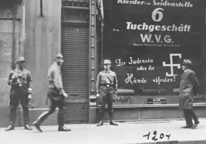 Des Stormtroopers nazis (Sturmabteilung ou SA) montent la garde devant une entreprise juive. Les graffitis peints sur la vitrine disent : « Que tes mains pourrissent, espèce de porc juif! »
