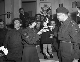 La caporale M. Freeman, du Corps féminin de l'armée canadienne (C.W.A.C.) et le capitaine H/Capitaine Samuel Cass, aumônier juif, remettent un cadeau à une jeune fille belge lors d'une célébration de Hanukkah, Tilberg, Pays-Bas, 17 décembre 1944.