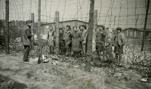 Un homme parle à un groupe de prisonniers séparés par deux grillages.