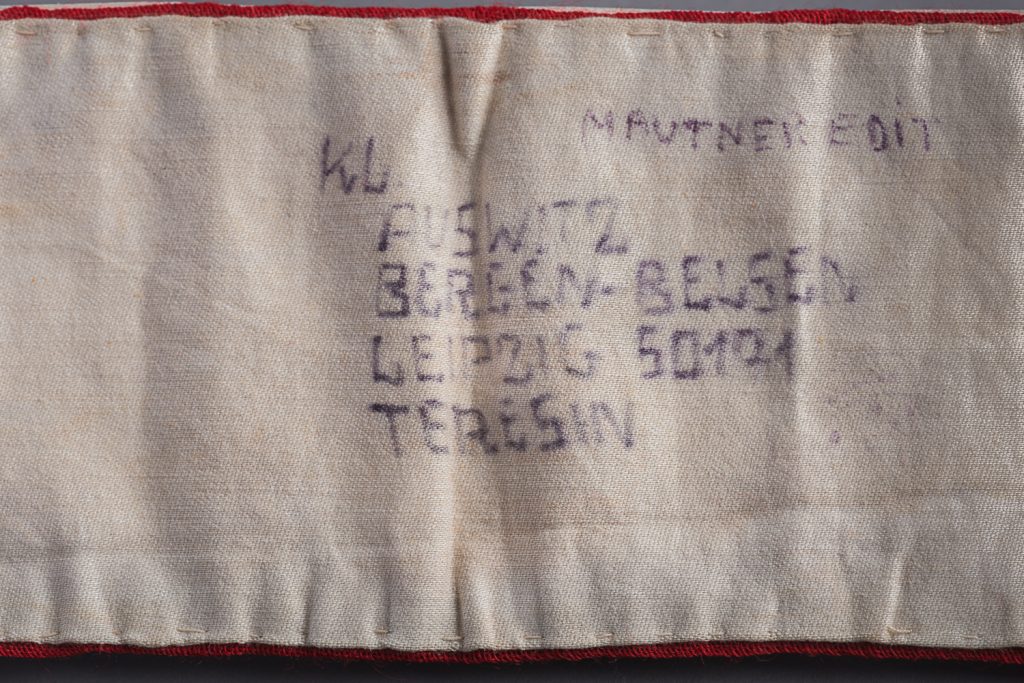 Ce brassard rouge recouvert d’un tissu blanc est marqué des noms de quatre camps : Auschwitz, Bergen-Belsen, Leipzig et Terezin. —Musée Holocauste Montréal.