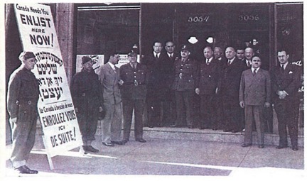 Un groupe d'hommes vêtus d'uniformes et de costumes militaires se tient devant un bâtiment avec un panneau écrit en anglais, en yiddish et en français pour attirer les recrues potentielles de l'armée.