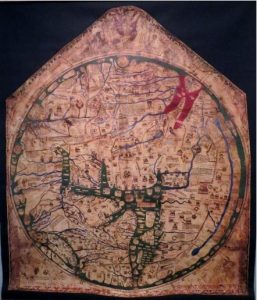 Photograph of a replica of a brown cloth map (Hereford Mappa Mundi, c. 1300) in a pentagonal shape with a point at the top and a circular map drawn inside. The map has blue, red, and green colours depicting water features as well as known and mythical places, with Jerusalem at the centre marked by a crucifix.