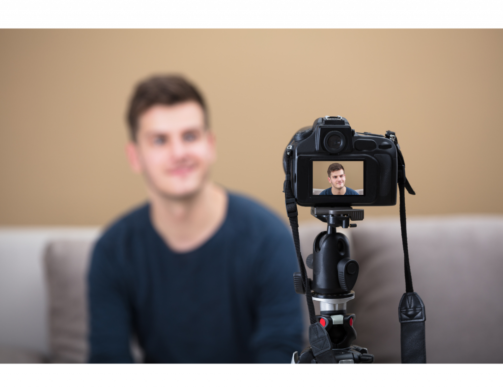 Image of a camera on a tripod recording a man sitting on a sofa