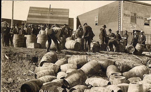 photo of a police raid at Elk Lake, Ontario, Canada, c. 1925. Showing some of the 160 kegs that were destroyed and a group of men outdoors in front of buildings.