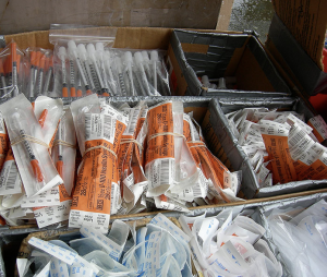 Packets of different sterile syringes. Some are in plastic ziplock type bags, others are bundled together by elastics.