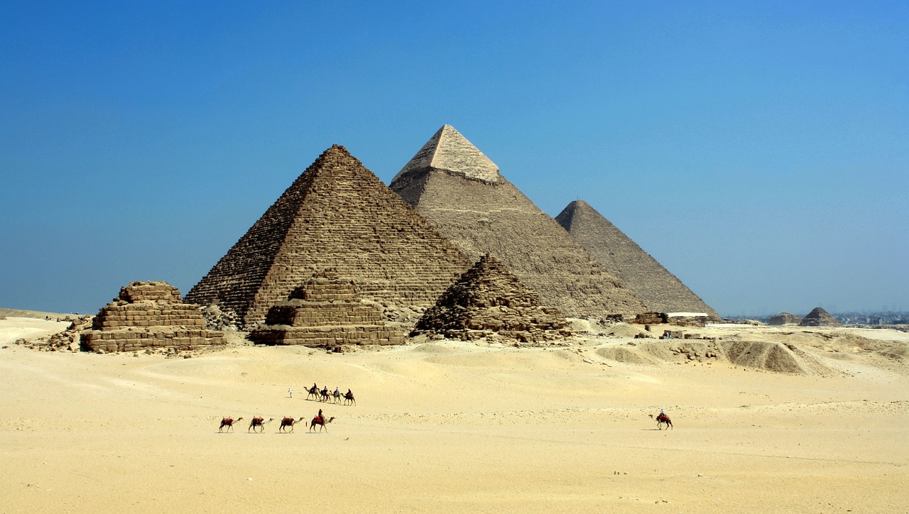 photo of 3 tall pyramids and 2 smaller pyramids in desert with strings of cameras in foreground