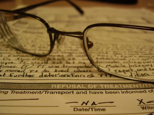 Paper form with handwriting on it with dark wire-framed glasses.