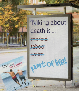 outdoor sign on sidewalk that says, "Talking about death is..." followed by strikethrough text for morbid, taboo, and weird, and part of life!