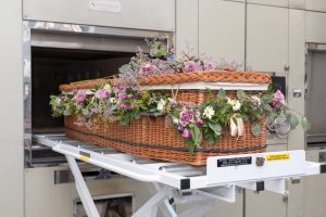 A willow coffin decorated with flowers is moved into a cremator.