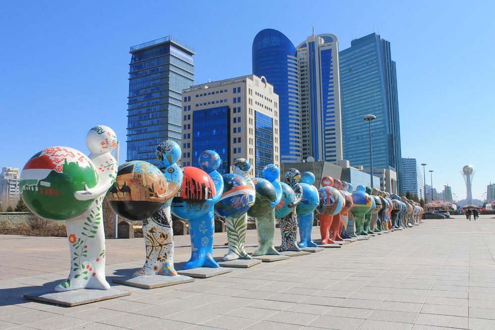 Colourful statues holding globes in front of tall office buildings