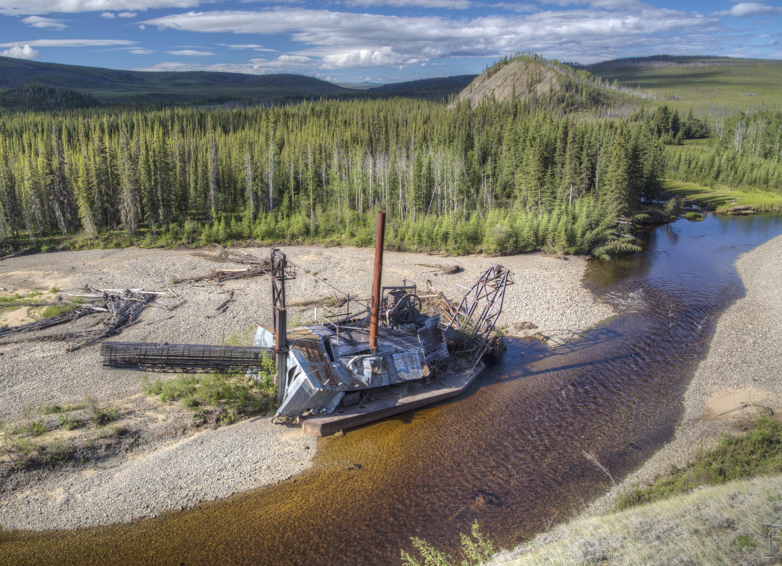 Collapse gold mining apparatus or dredging platform, along the rocky bank of a shallow stream.