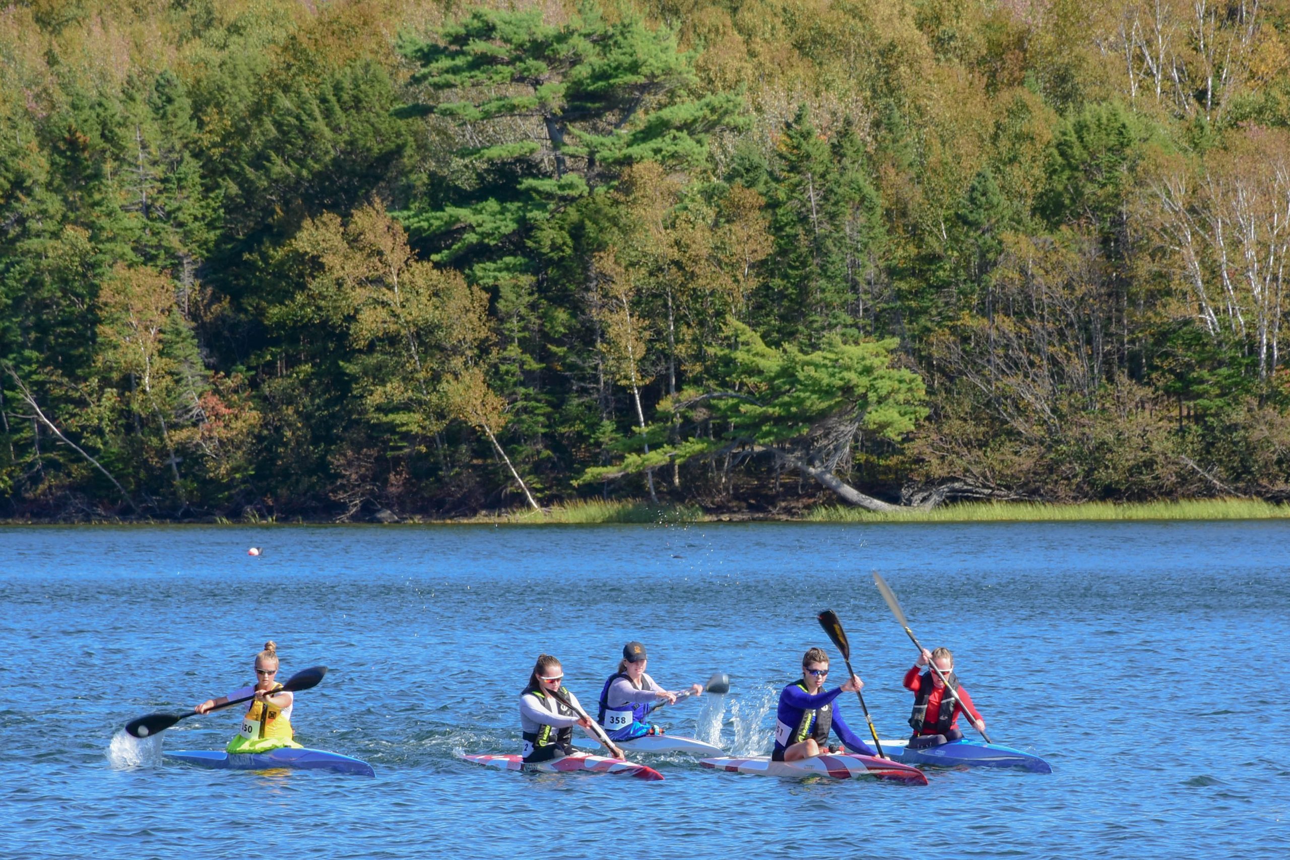 Kayakers on a lake in autumn. Deciduous trees in fall colours on the opposite shore.