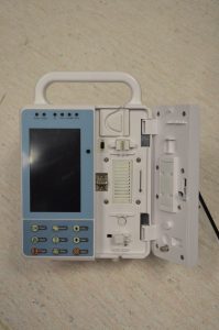 Alt text Photo of an Infusion Pump (Advance Medical) found in the Biomedical Engineering laboratory. The photo depicts the front view of an infusion pump with the door open showing where the syringe would be placed (no syringe in picture).