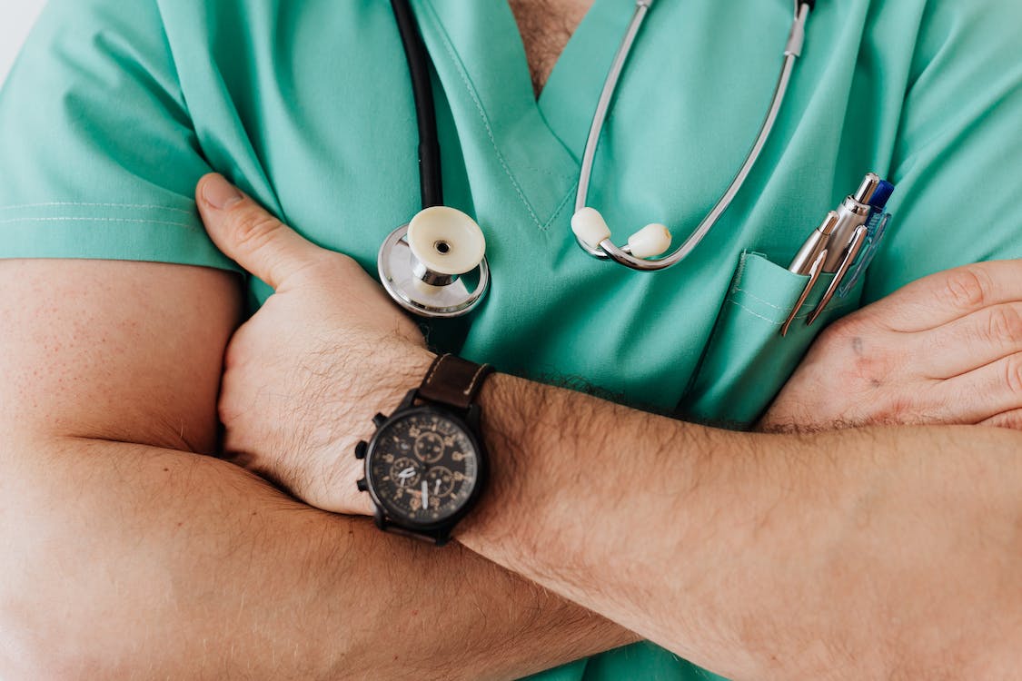 A healthcare worker in a green medical uniform, with his arms crossed.