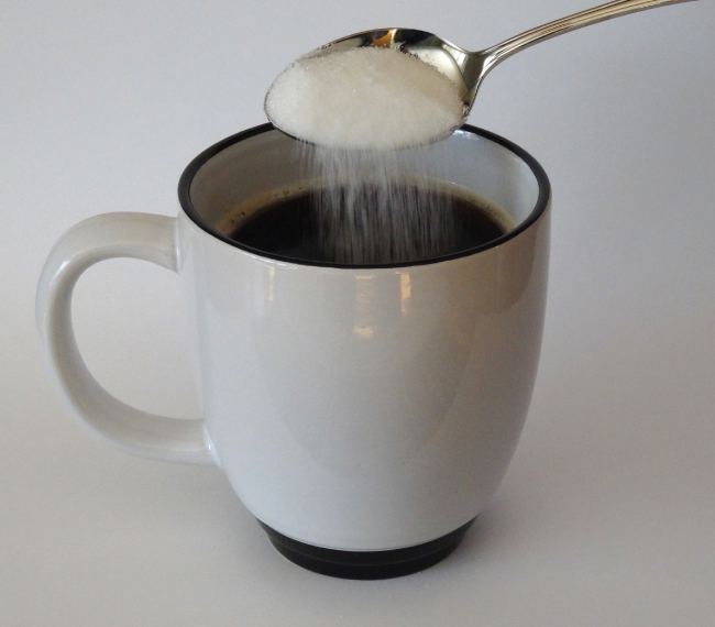 A picture is shown of sugar being poured from a spoon into a cup of coffee.