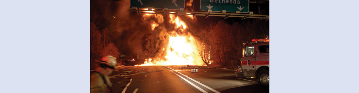 A photograph of a large ball of fire burning on a road. A fire truck and fireman are shown in the foreground.