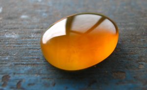 A photograph of a piece of gold-colored amber that has been rubbed and polished to a smooth, rounded shape.