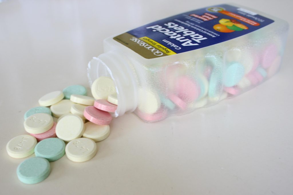 Image of a Jar of Antacid Tablets with lid off, laying on its side, with the green, yellow, and pink antacid tablets spilling out of the jar.