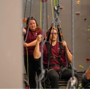 Photographs of climbing wall staff demonstrating and using the adaptive climbing equipment.