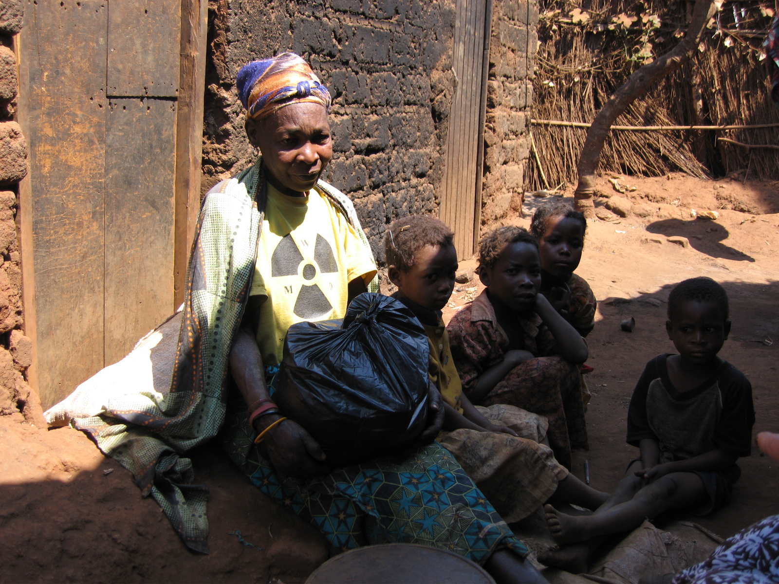 Older African woman sitting on the ground surrounded by four young children.