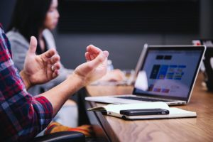 Hands of a person having a discussion with an open laptop in the background.