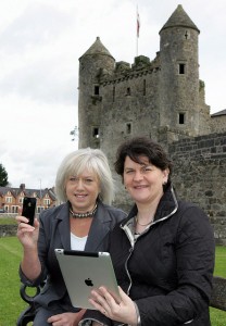 Two woman in front of an old castle. The woman on a right holds an ipad.