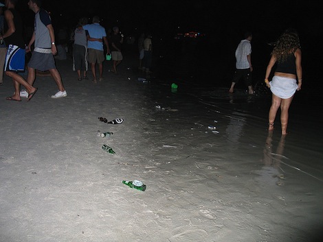 Young people on a beach at night drinking with beer bottles lying in the sand.